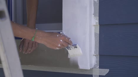 Slow-motion-shot-of-person-painting-window-frame-with-brush-on-wooden-house-outdoors---Renovation-of-house-facade