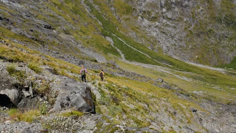 Pan-shot-of-hiker-couple-hiking-downhill-steep-green-mountains-on-during-sunny-day-at-Gertrude-Saddle