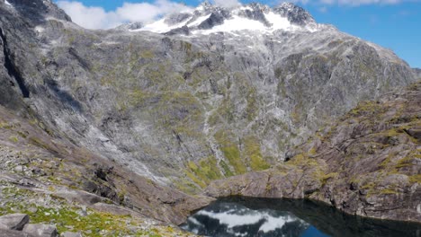 Antenne-Nach-Unten-Geneigt-Erschossen-Massive-Berge-Mit-Schneebedeckten-Gipfeln,-Die-Sich-Bei-Sonnenlicht-In-Der-Natürlichen-Bergseeoberfläche-Spiegeln---Gertrude-Sattelwanderung-In-Neuseeland