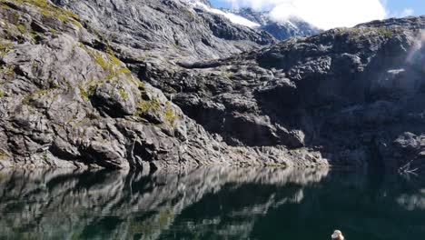 Persona-Descansando-En-La-Orilla-Del-Lago-Y-Disfrutando-De-Una-Vista-Espectacular-De-La-Montaña-Durante-El-Día-Soleado-Y-El-Cielo-Azul---Pista-De-Sillín-Getrude-En-Nueva-Zelanda---Vista-Trasera