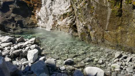 Zeitlupenaufnahme-Eines-Frischen-Wasserfalls,-Der-Während-Eines-Sonnigen-Tages-Bei-Gertrude-Saddle,-Neuseeland,-In-Einen-Klaren-Fluss-Fließt