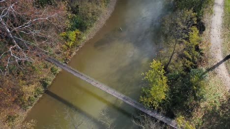 Toma-De-Drones-De-Un-Puente-Colgante-Sobre-Un-Río-En-El-Bosque-Durante-La-Temporada-De-Otoño