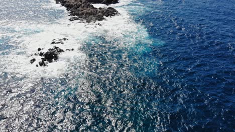 Top-Down-View-Of-Foamy-Sea-Waves-Splashing-On-Rocks-In-The-Middle-Of-The-Ocean---aerial-drone-shot