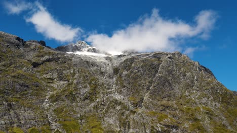 Low-angle-view-of-white-clouds-flying-over-mountain-peak-in-Fiordland-National-Park-of-New-Zealand-in-Summer