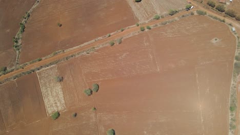 Top-down-aerial-over-arid-farmlands-and-cars-parked-on-dirt-roads