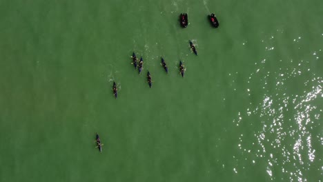 Aerial-drone-view-rotating-shot-of-a-rowing-team-of-sport-kayak-practicing-with-black-boats-in-the-ocean-on-a-sunny-day
