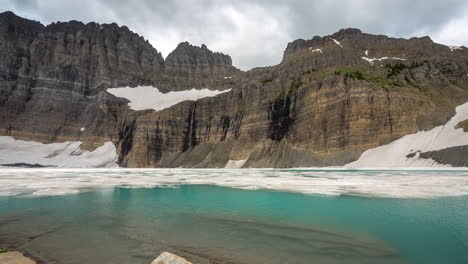 Time-Lapse,-Glacier-and-Glacial-Iceberg-Lake-Under-Steep-Cliffs,-Clouds-and-Snow-in-Landscape-of-Glacier-National-Park,-Mount-Grinnell