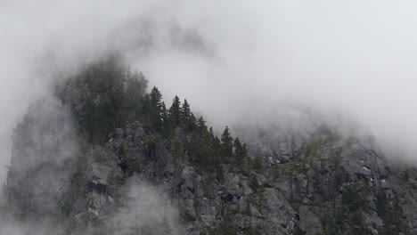 Mist-gently-rolling-over-forest-trees-on-mountain-cliff-in-British-Columbia,-aerial