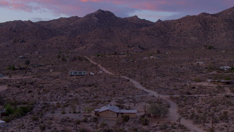 Slow-rise-over-homes-and-lonely-old-dirt-road-at-sunset-in-Joshua-Tree,-California