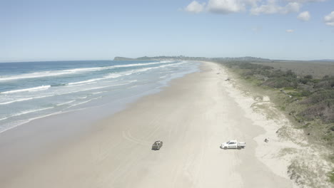 4k-Wide-drone-shot-of-a-tourist-car-driving-on-a-long-hot-beach-in-Australia