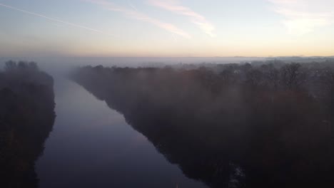 Dense-fog-misty-Autumn-Manchester-ship-canal-aerial-view-above-silhouette-treetops