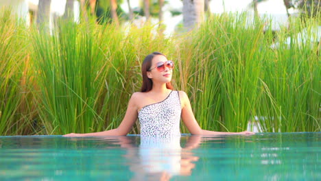 Fashionable-Korean-Woman-in-Blotchy-One-shoulder-Monokini-Relaxing-In-Swimming-Pool-Water-Leaning-on-Pool's-Border-Edge-in-the-tropical-Hotel-lounge-in-Malaysia,-static-slow-motion
