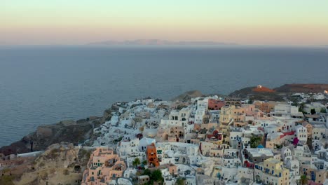 Aerial-flyover-Famous-Destination,-Charming-Oia-town-at-Sunrise-lights,-Santorini
