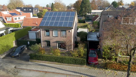 Jib-down-of-small-detached-house-with-a-rooftop-filled-with-solar-panels-and-an-electric-car-charging-in-parking-lot