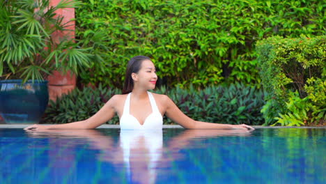 Frau,-Die-Sich-Im-Schwimmbadwasser-Entspannt-Und-Sich-An-Den-Rand-Des-Pools-In-Einer-Tropischen-Hotellounge-In-Indonesien-Lehnt,-Statische-Zeitlupe