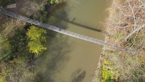 Person-crosses-a-suspension-bridge-over-a-river-during-the-autumn-season
