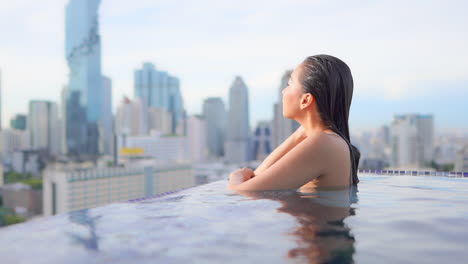 Eine-Junge-Frau-Im-überlaufpool-Auf-Dem-Dach-Auf-Einem-Erstaunlich-Verschwommenen-Stadtbildhintergrund-Von-Bangkok,-Der-Den-Sonnenuntergang-Genießt