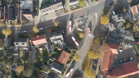 Top-down-aerial-of-buses-leaving-small-busstation-in-a-small-town-in-autumn
