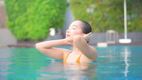 Passionate-Asian-Girl-Touches-her-Wet-Hair-inside-the-swimming-pool-of-an-exotic-hotel-daytime,-static-portrait-shot