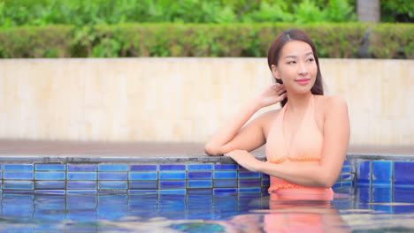 A-pretty-young-woman-leans-on-her-elbow-on-the-edge-of-the-swimming-pool,-turns-her-head,-and-smiles