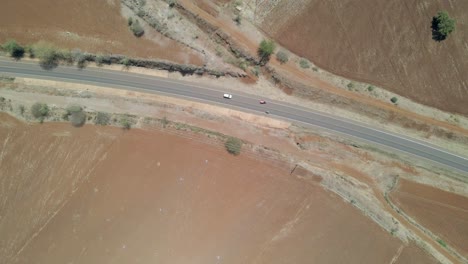 Top-down-aerial-of-traffic-driving-over-calm-highway-in-rustic-Kenyan-countryside