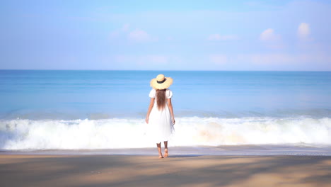 Woman-in-white-summer-dress-standing-on-the-beach-by-the-sea-and-raising-arms-up-faces-endless-seascape---vacation-template-back-view