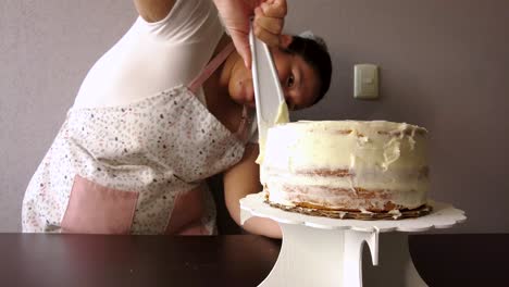 Latin-woman-wearing-an-apron-preparing-cooking-baking-a-cake-spreading-the-butter-frosting-with-a-white-spatula