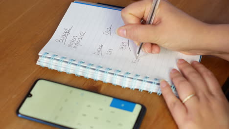 Mujer-Calculando-El-Presupuesto-De-Finanzas-Familiares-En-Calculadora-Y-Escribiendo-En-Cuaderno