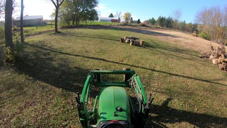 High-angle-point-of-view-on-small-green-tractor-driving-maneuvering-towards-a-pile-of-stumps