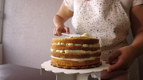 Latin-woman-wearing-an-apron-preparing-cooking-baking-a-cake-adding-butter-frosting-with-a-white-cake-scraper