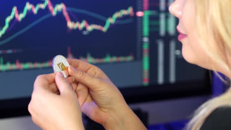 Blonde-woman-holding-and-looking-at-ethereum-coin-in-her-hands-in-front-of-cryptocurrency-trading-graphs