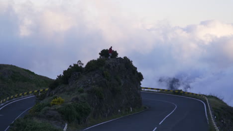 Man-walks-to-point-above-stunning-hairpin-turn-on-cloudy-mountain-highway