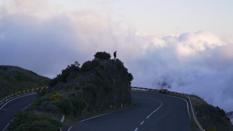 Silhouetted-man-standing-above-beautiful-hairpin-turn-on-foggy-mountain-highway