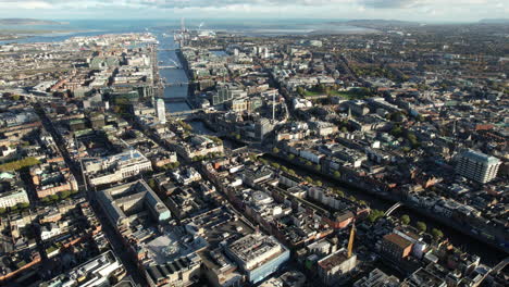 Downtown-Dublin,-Ireland,-High-Rise-Aerial-View-of-Cityscape,-Buildings,-Liffey-River-and-Skyline-on-Bay-on-Sunny-Day,-Drone-Shot