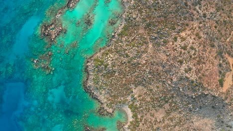 Top-down-view-crystal-clear-turquoise-water-with-rocky-Coastline,-Crete-island