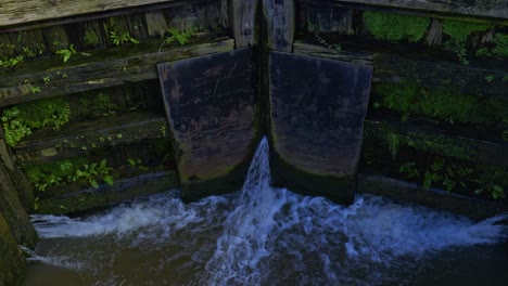 Canal-lock-with-water-pouring-throuigh-large-wooden-gates-into-old-barge-narrowboat-lift-system