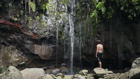 Panning-up-to-man-on-rock-gazing-at-small-waterfall-in-flourishing-jungle