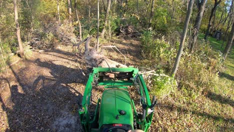 High-angle-point-of-view-on-small-green-tractor-using-lift-forks-to-move-a-tree-stump
