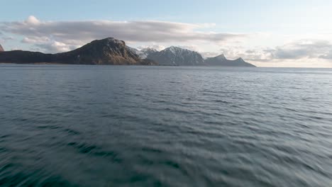Drone-flies-low-over-sea-towards-mountains-at-lofoten-islan-in-northern-Norway