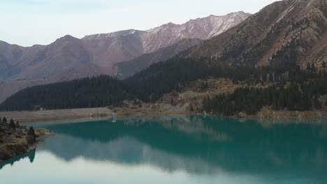 Side-drone-footage-of-the-turquoise-colored-lake-water-at-Big-Almaty-Lake-and-the-Trans-Ili-Alatau-mountains-in-Kazakhstan
