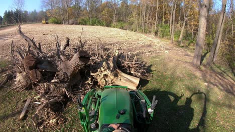 High-angle-point-of-view-on-small-green-tractor-using-lift-forks-to-pickup-a-tree-stump-from-a-pile