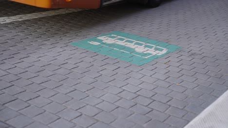 Electric-bus-leaving-the-energy-station-after-recharging-the-battery,-passing-the-charging-logo-sign-on-the-ground