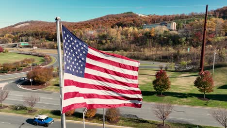 Proud-American-flag-waves-in-wind-beside-road-during-autumn-fall-foliage