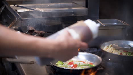 Working-restaurant-kitchen,-chef-adds-sauce-to-various-orders-with-squeeze-bottle,-a-variety-of-dishes-cook-on-stove-top-in-traditional-commercial-restaurant-kitchen,-slow-motion-slider-HD