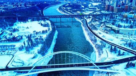 4k-Winter-Aerial-Loop-hold-birds-view-over-the-Walter-Dale-Bridge-as-ice-pieces-flow-down-North-Saskatchewan-River,-with-light-traffic-crosses-North-to-the-downtown-core-in-between-to-major-parks3-3