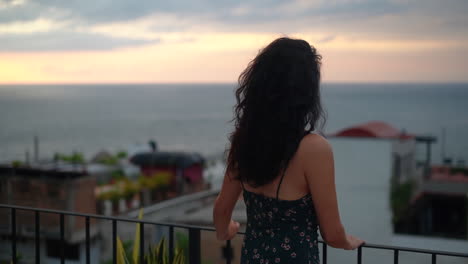 Young,-brunette-woman-watching-the-sunset-over-the-ocean-from-the-rooftop---pull-back-rack-focus