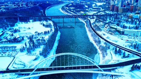 4k-Winter-Aerial-hold-birds-view-over-the-Walter-Dale-Bridge-as-ice-pieces-flow-down-North-Saskatchewan-River,-with-the-Vintage-old-High-level-bridge-in-the-horizon,-by-Victoria-and-Kinsmen-parks2-3