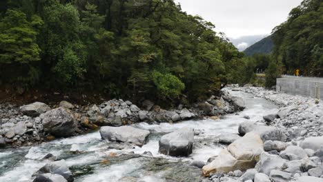 Tranquil-flowing-river-between-rocks-and-boulders-surrounded-by-dense-rainforest---Falls-Creek,New-Zealand