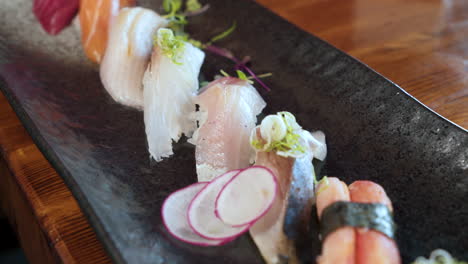 Los-Palillos-Recogen-Un-Trozo-De-Sushi-De-Un-Colorido-Plato-De-Nigiri-Tradicional-En-Un-Restaurante-Japonés,-Deslizador-De-Cerca-4k
