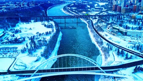 4k-Winter-Aerial-hold-birds-view-over-the-Walter-Dale-Bridge-as-ice-pieces-flow-down-North-Saskatchewan-River,-with-the-Vintage-old-High-level-bridge-in-the-horizon,-while-snow-covers-both-parks1-3